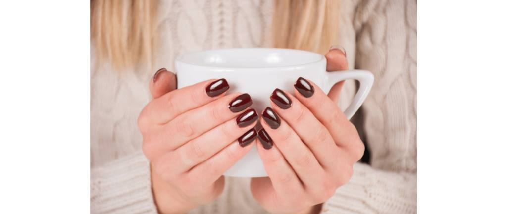 Mãos de mulher com esmalte marrom segurando uma xícara de chá