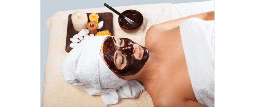 Mulher relaxando com máscara de argila preta aplicada no rosto deitada de toalha no cabelo e corpo